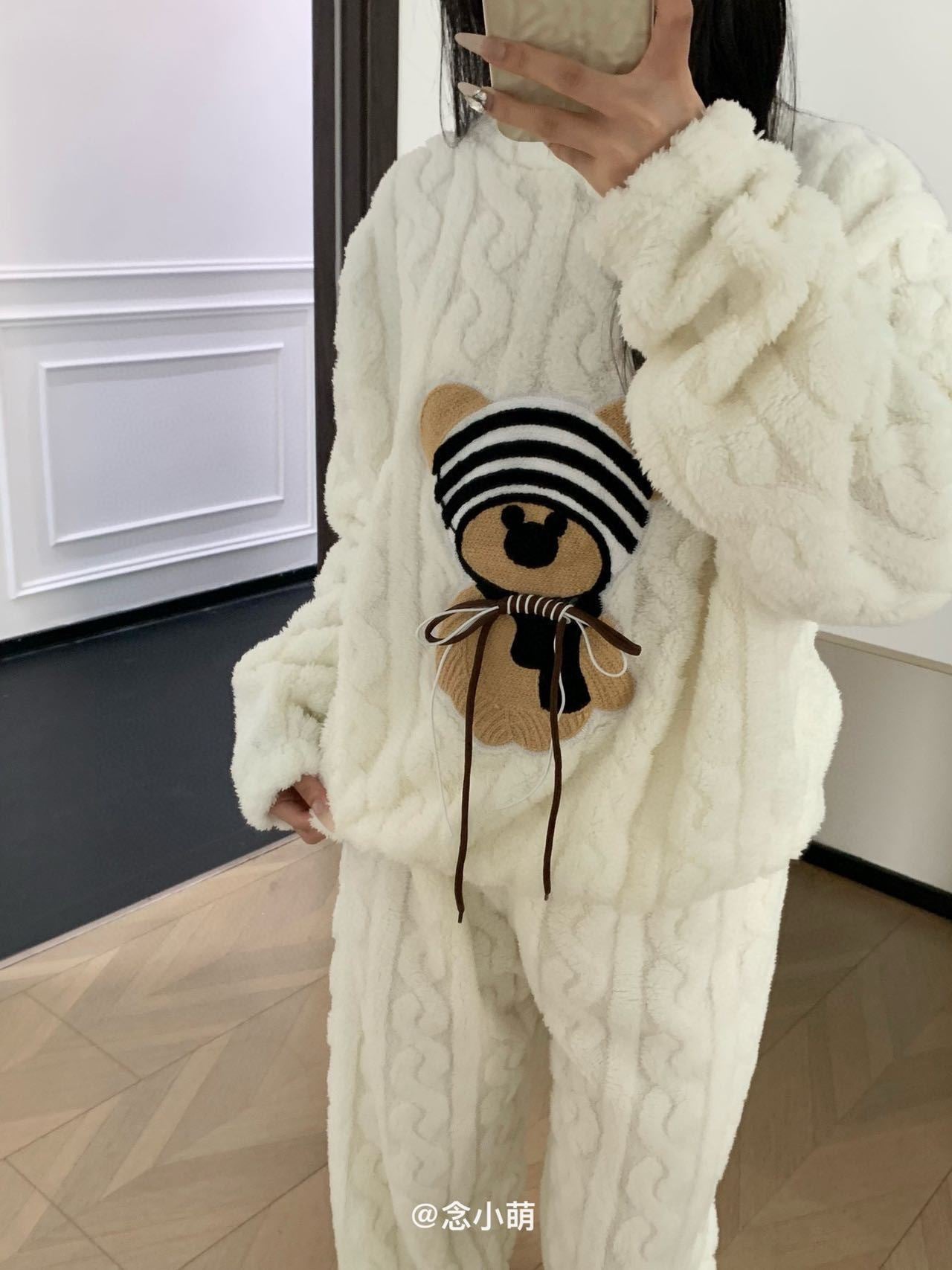 Person wearing a white cable knit sweater and pants holding a small bag with a bear design